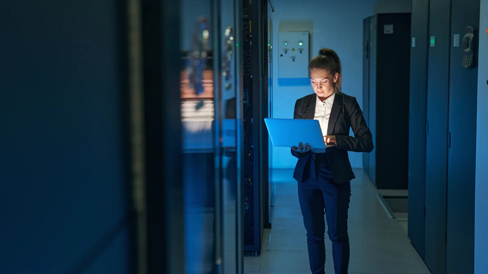 Technikerin mit Laptop in einem dunklen Serverraum bei der Wartung