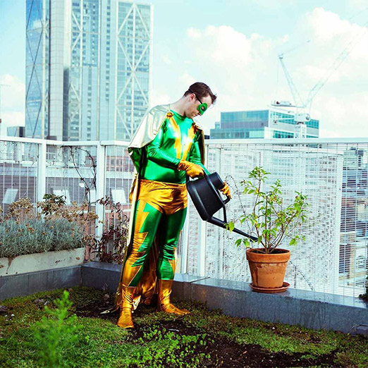 Superheld gießt eine Pflanze auf einer Dachterrasse - symbolisiert sorgfältige Pflege und Wachstum digitaler Projekte
