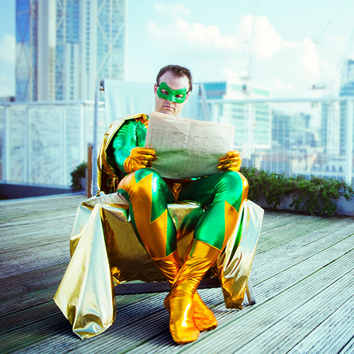 Superheld ließt eine Zeitung auf einer Dachterrasse in einem gemütlichen Stuhl - symbolisiert entspannte Haltung